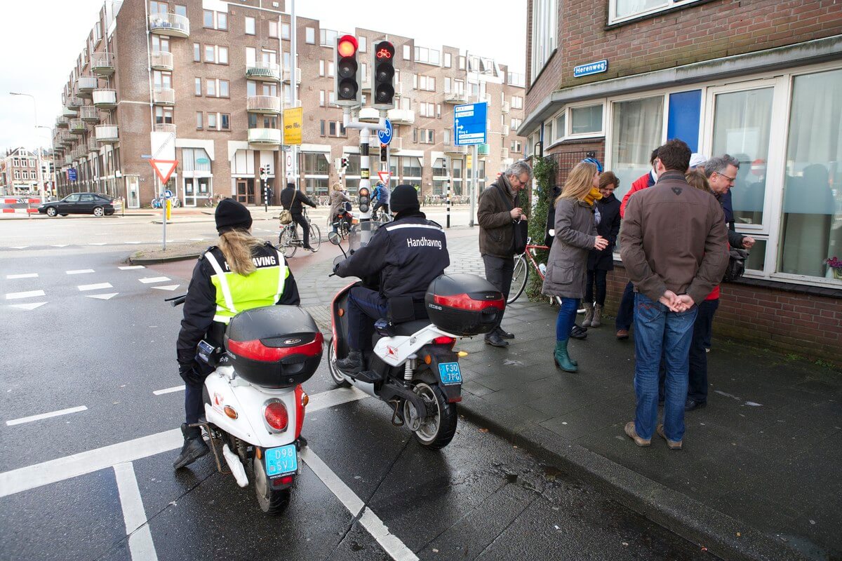 Toezichthouders staan netjes te wachten voor het rode fietsverkeerslicht bij de Oudenoord dat verkeerswethouder Van Hooijdonk overbodig vindt. Foto: Ton van den Berg