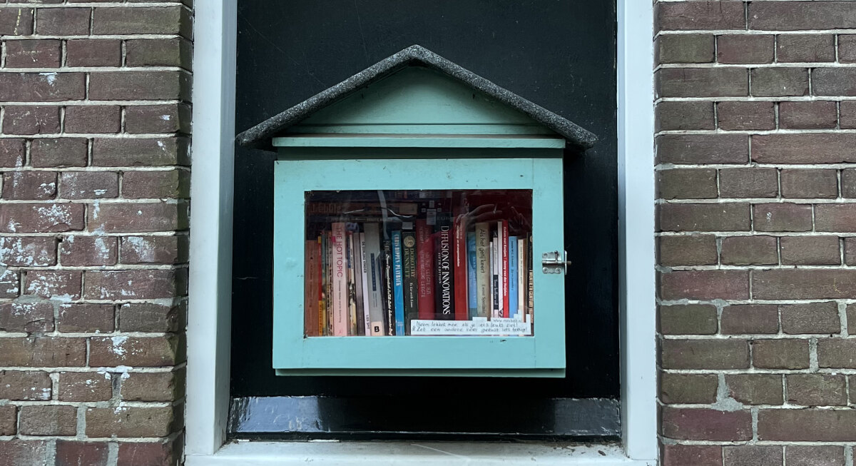 In een dichtgemaakt raam hangt een klein, turquoise boekenkastje met puntdak. Foto: EvA
