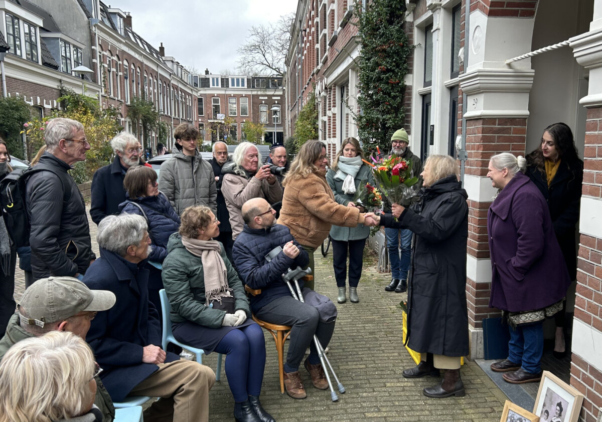 Marleen, die de steentjes voor haar grootouders aanvroeg, geeft bloemen aan de huidige bewoonster van het pand (foto: JT)