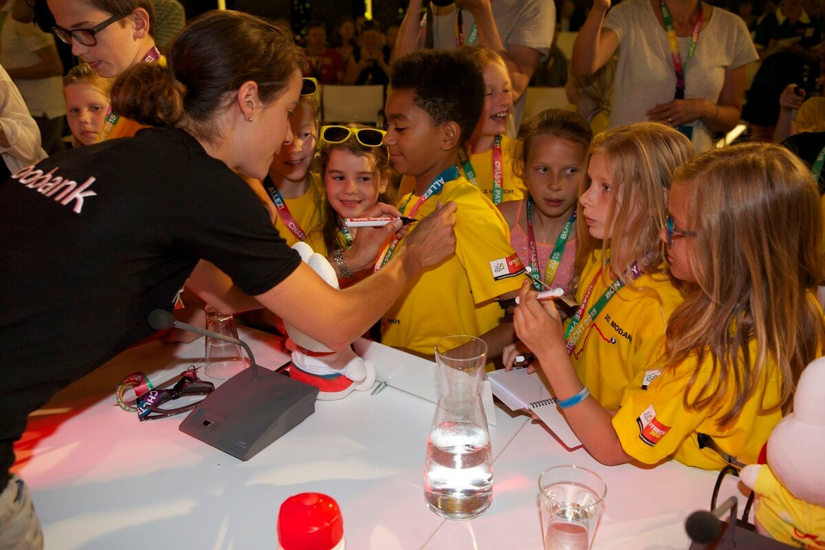 Marianne Vos zet een handtekening op een shirt van een deelnemer aan de kinderpersconferentie. Foto: Ton van den Berg