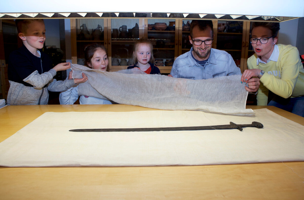 Vlnr: Joep, Jet, Pip, Mark en Kim Jongerius onthullen het in de Kromme Rijn gevonden zwaard. Foto: Ton van den Berg