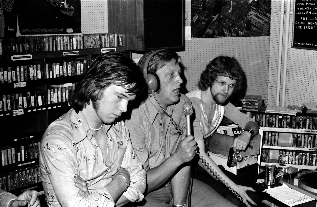 Op het schip van Radio Noordzee, de MEBO II (31 augustus 1974) met links John de Mol jr. (technicus), midden John de Mol sr. (dir. Radio Noordzee) en rechts Marc van Amstel. Foto: Archief Van Amstel