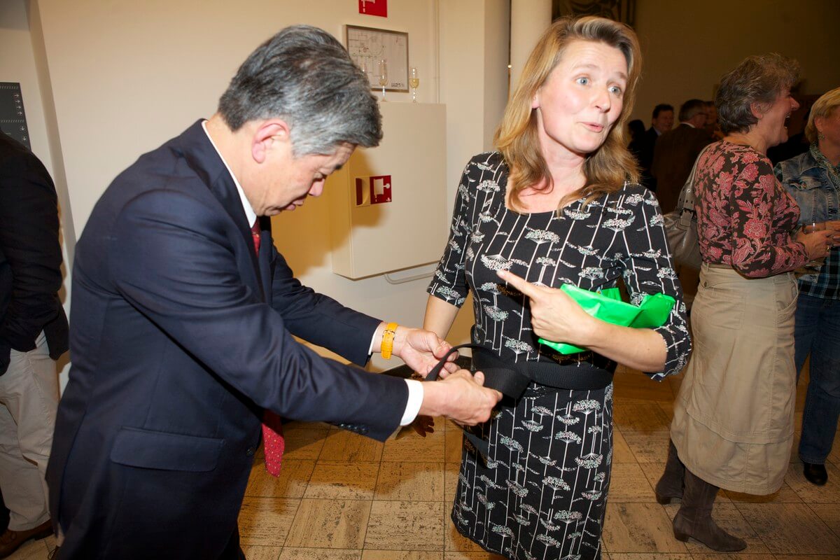 Een medewerker van de Japanse ambassade knoopt een zwarte band om Roosje Keijzer, samensteller van de Geesinkexpositie. Foto: Ton van den Berg 
