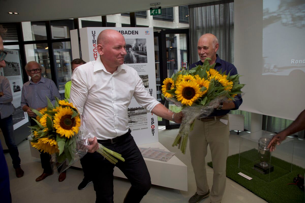 Organisator van de expositie Remco Neu deelt zonnebloemen uit aan Leo van Veen. Foto: Ton van den Berg