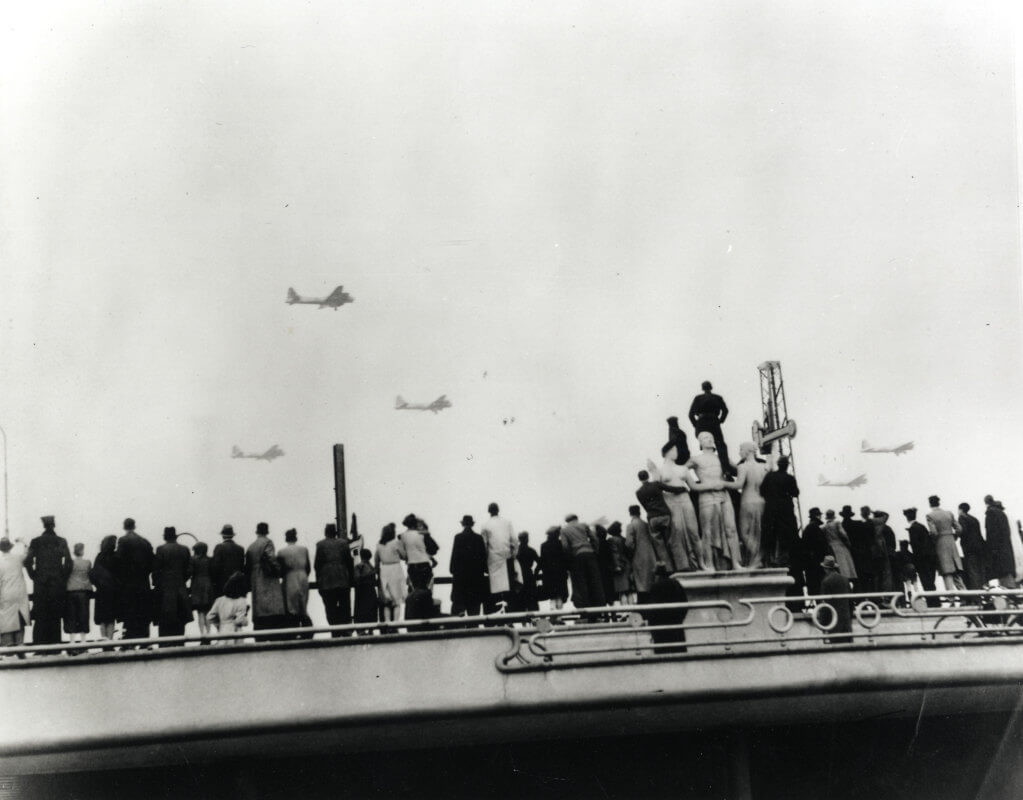 Utrechters beklimmen het beeld van Gerrit van der Veen om de vliegtuigen vol met voedsel over te zien vliegen, begin mei 1945. Fotograaf is onbekend, collectie HUA