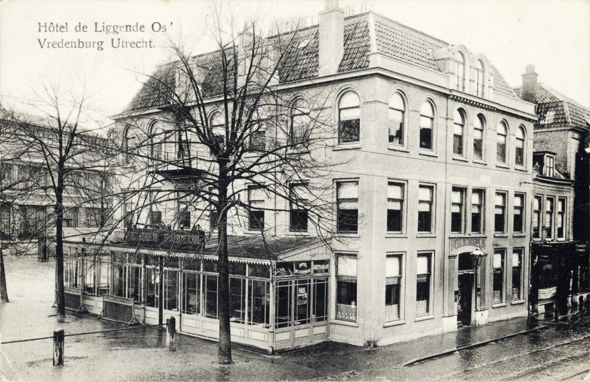 Op deze foto uit ongeveer 1911/12 zien we “De Liggende Os” zoals het eruit zag na de verbouwing die in 1910 plaatsgevonden had. Duidelijk te zien dat er een verdieping bijgekomen is. Omdat er ook kamers op zolder werden verhuurd, moest er een ontsnapping bij brand mogelijk zijn. Die	zien we tegen de oostzijde gerealiseerd.