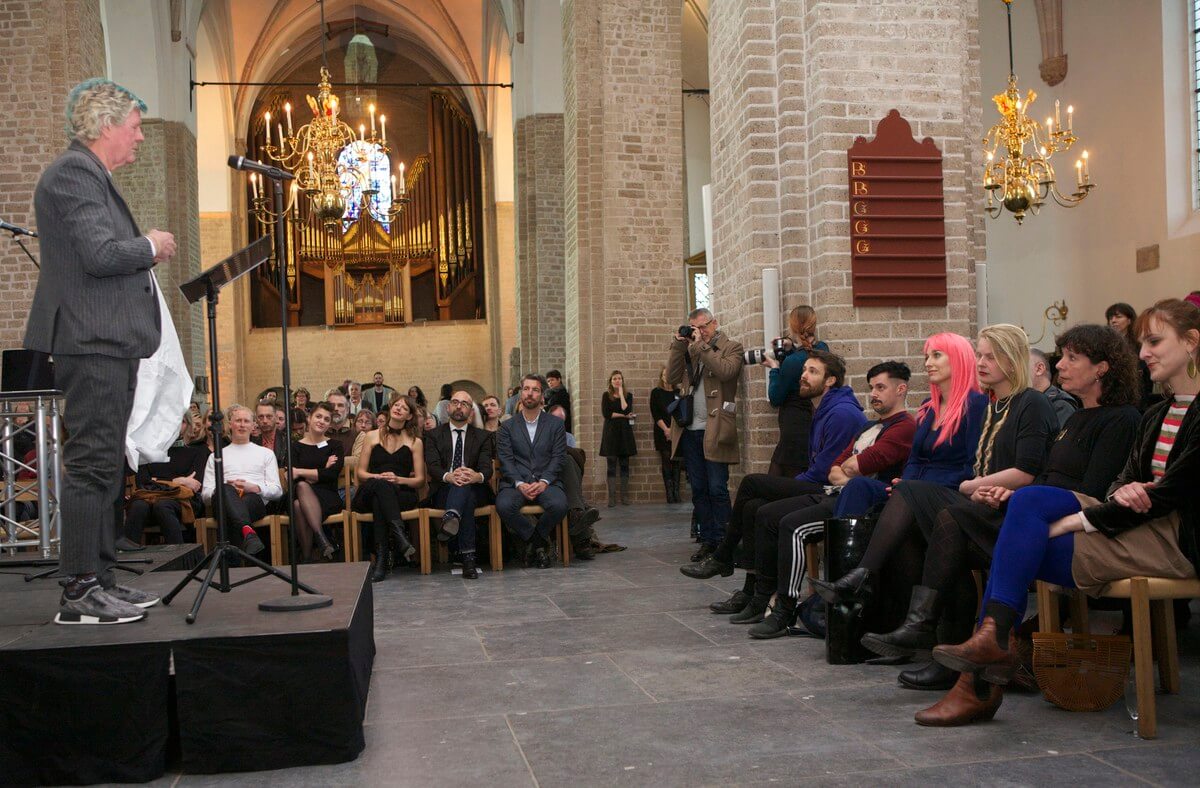 Christiaan spreekt bij de opening van de expositie de kunstenaars (voorste rij) toe. Foto: Ton van den Berg