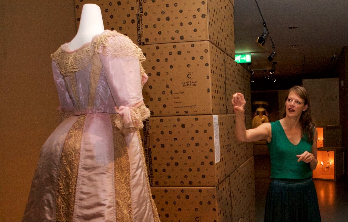 Modeconservator Ninke Bloemberg bij een japon uit 1902 die speciaal voor de expositie is gerestaureerd. Foto: Ton van den Berg