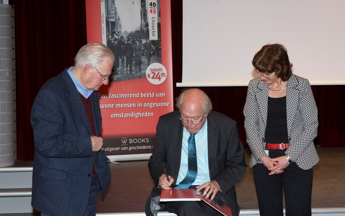 Van Liempt een handtekening in het boek van Burkunk en directeur Chantal Keijsper van Het Utrechts Archief kijkt toe.