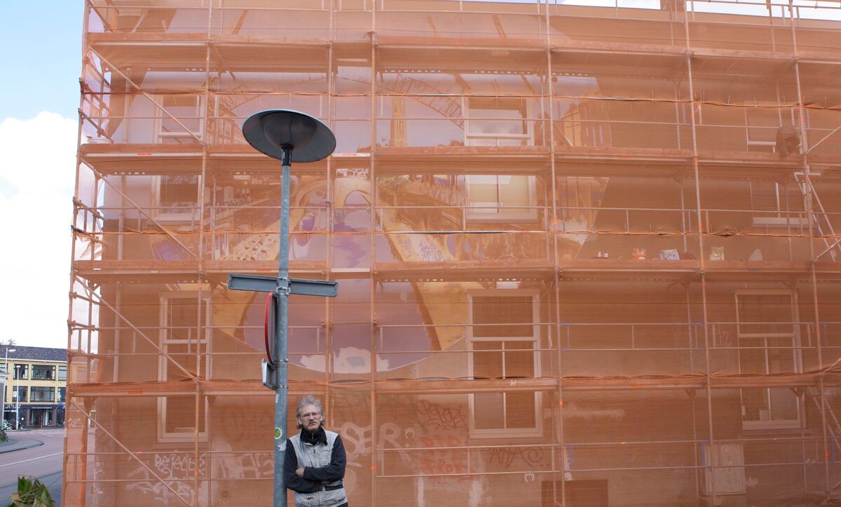 Peeters voor de stellage waarachter zijn muurschildering zich bevindt. 