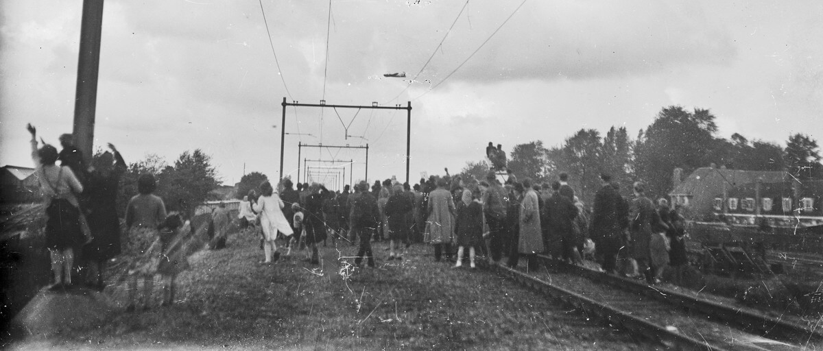 Publiek zwaait en kijkt op de spoorlijn naar een overvliegend vliegtuig. Foto: Frans Beenen