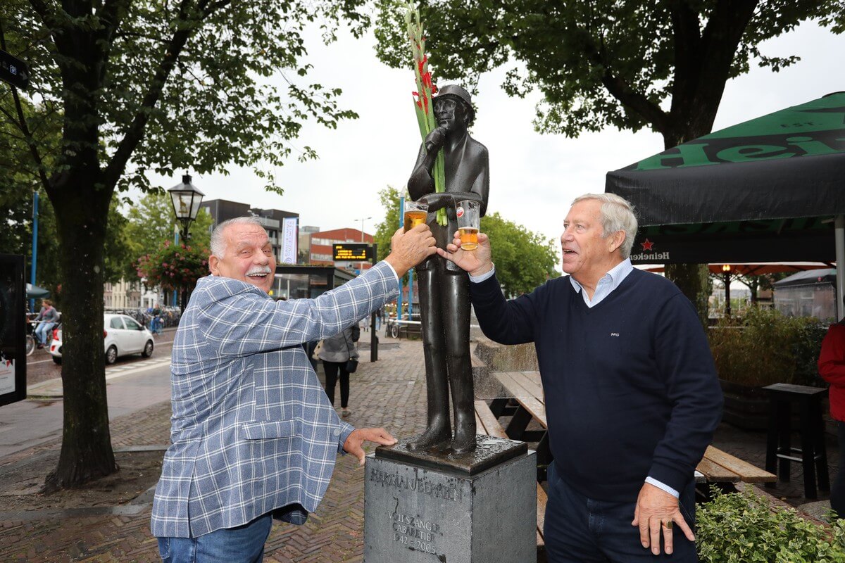 Harry Roestenburg en Jan Stekelenburg, jeugdvrienden van Herman, proosten bij het beeld van Herman Berkien (gemaakt door Frans Stelling). Foto: Ton van den Berg