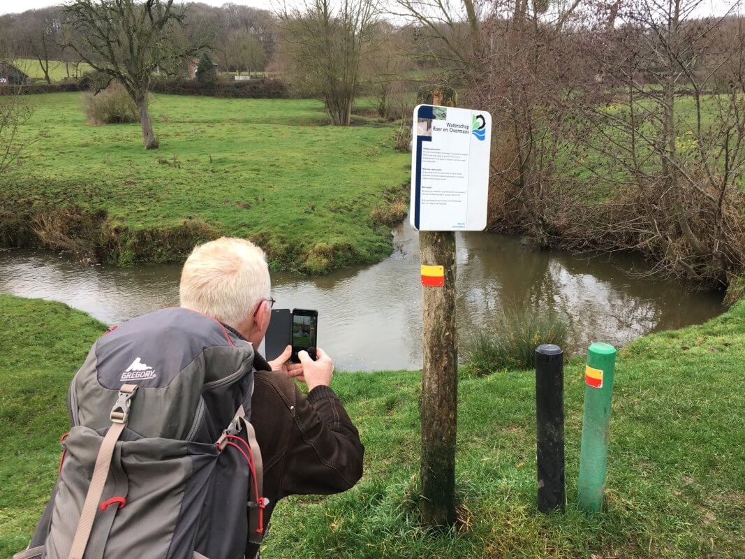 Kees gehurkt voor bord met geelrode wandelmarkering op paal. Foto: Dik Binnendijk