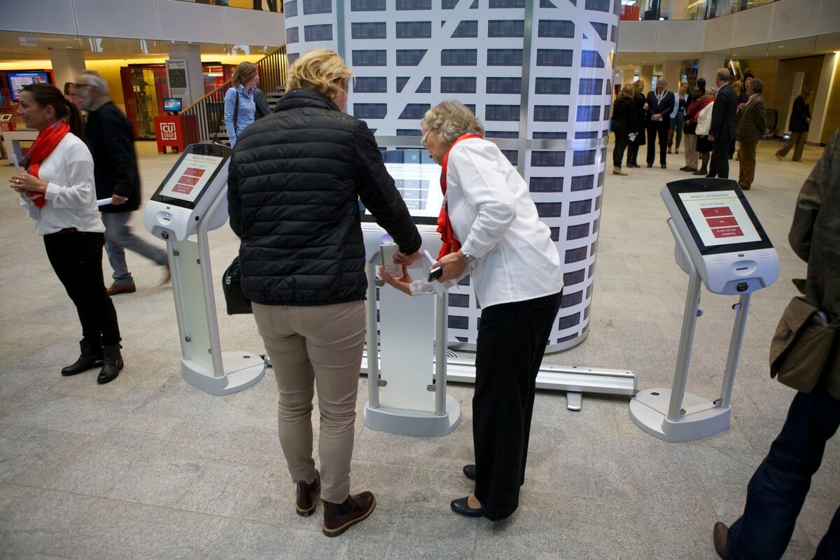 Publieksmedewerkers helpen bij het aanmelden op een console in de hal. Foto: Ton van den Berg