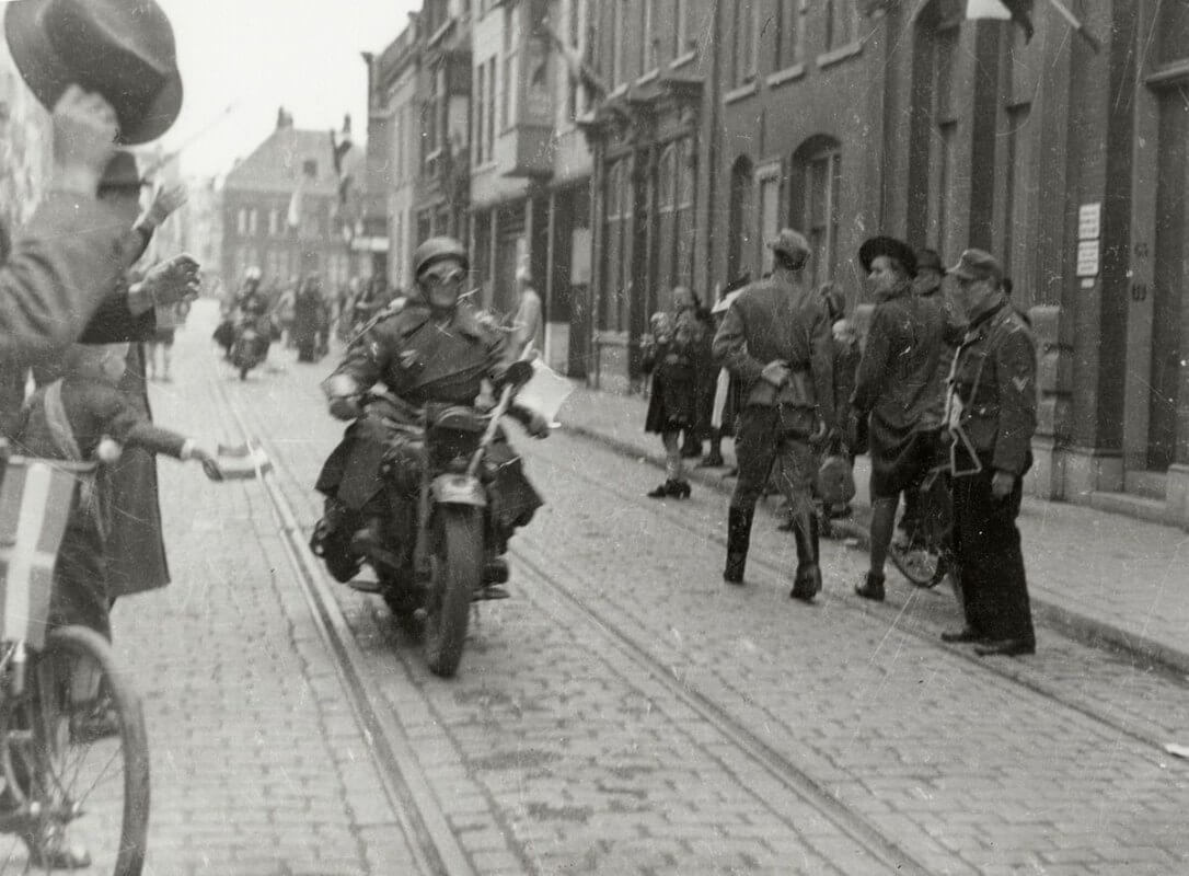 Drie Canadese motorrijders in de Voorstraat op weg naar het Academisch ziekenhuis worden toegejuicht, een Duitse soldaat met mitrailleur staart naar wat er voorbij komt. Foto: Collectie HUA
