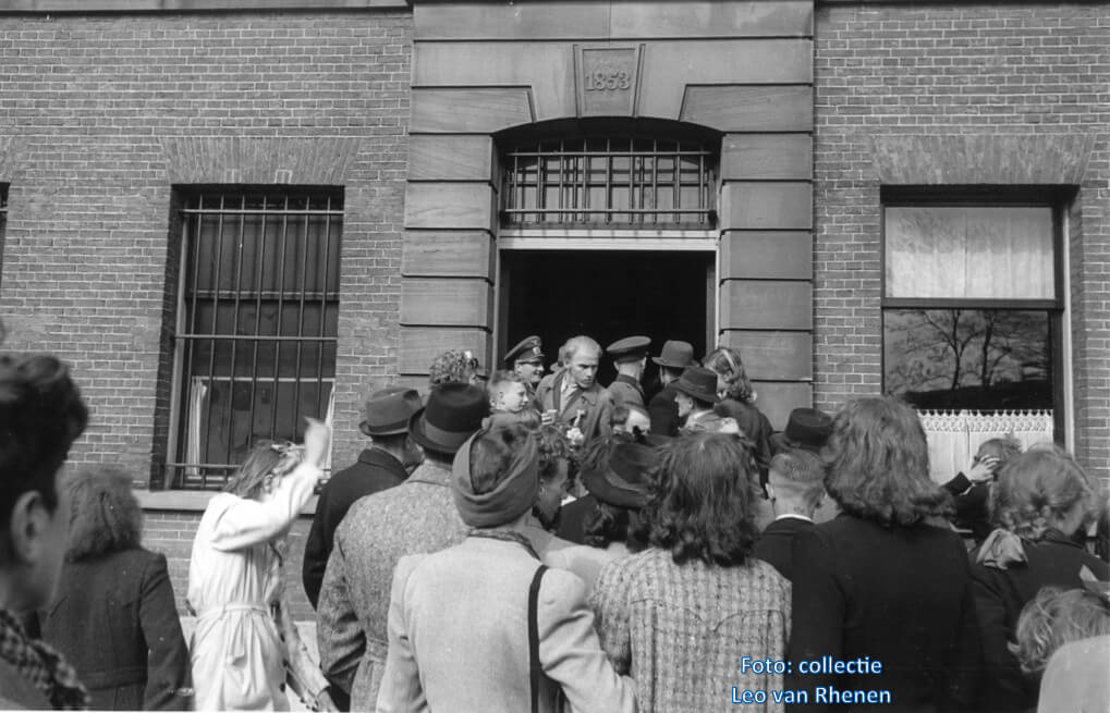 Een vrijgelaten gevangene wringt zich langs Duitse soldaten naar buiten waar vrouwen en kinderen reikhalzend uitkijken naar hun echtgenoot, broer, zoon of vader. Foto: Collectie Leo van Rhenen
