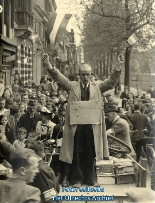 De 'kampbeul van Amersfoort' wordt gedwongen zijn handen in de lucht te houden en met vlaggetjes te zwaaien. Foto: G.J. Lauwers (Collectie HUA)